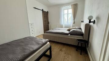 Una habitación pequeña y limpia con cama, una silla, cómoda y ventana con cortinas.