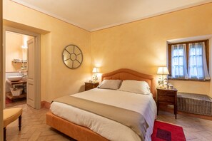 A bedroom with a large bed, bedside tables, a wall clock, a window with curtains, and a bathroom with a sink and shelves. - Apartment 'La Terrazza, Cetona, Toscana' with Mountain View, Wi-Fi and Air Conditioning (Cetona)