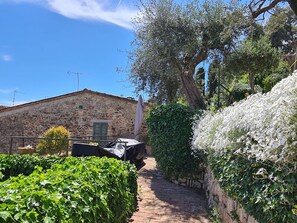 Un edificio de piedra con techo inclinado, un estrecho sendero de piedra y abundante vegetación.
