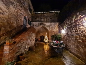 A stone courtyard with an arched entrance, a table with chairs, and potted plants.