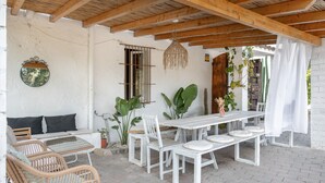A covered patio with a white table and chairs, a hanging light fixture, and potted plants.