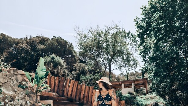A person sitting in a pool with a wooden deck and greenery in the background.