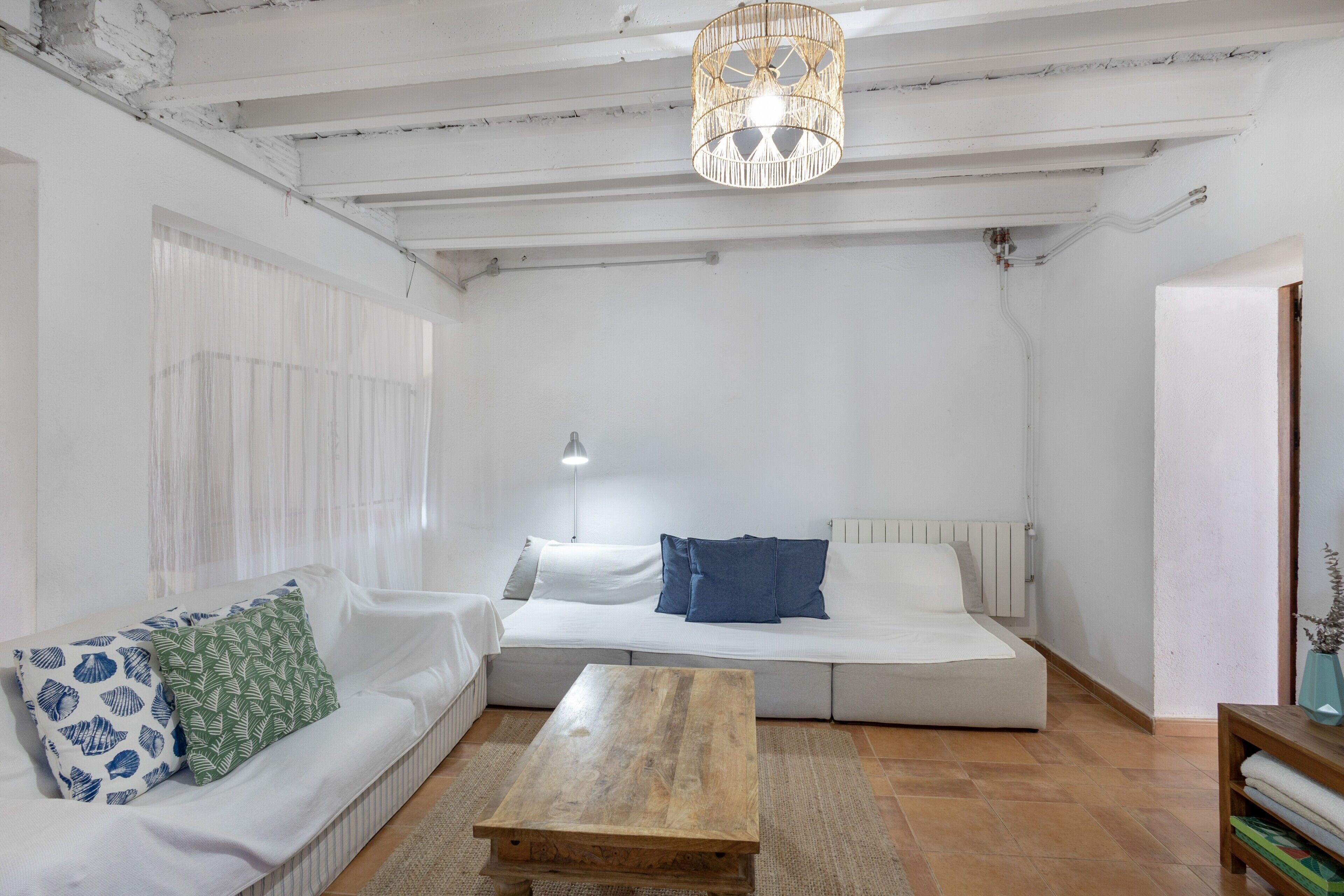 A room with a white sofa, a wooden coffee table, a hanging light fixture, and a radiator.