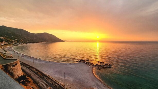 Une vue sur le coucher de soleil le long de la côte, avec une plage, une route sinueuse et un mur de pierres.