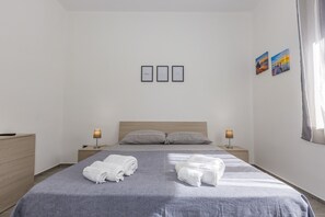 Une chambre d’hôtel avec un lit, deux tables de chevet, une commode et trois tableaux encadrés au mur.