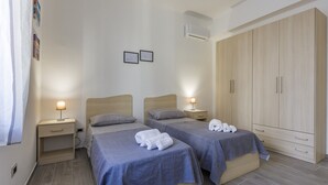Une chambre avec deux lits, des tables de chevet, une armoire et un climatiseur fixé au mur.