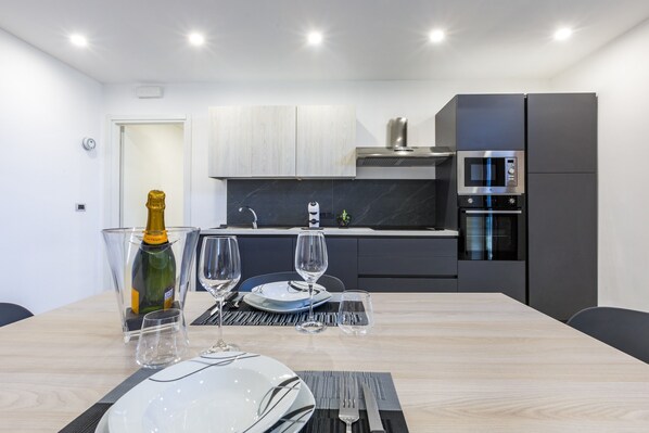 A modern kitchen with a dining table set for two, a microwave, and a built-in oven.