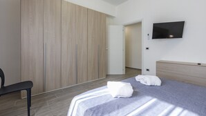 Une chambre à coucher moderne avec un lit, une télévision, une armoire et une chaise.