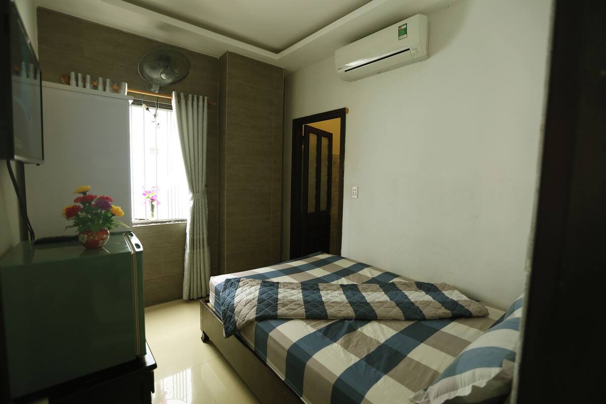 Un dormitorio con cama, cómoda, ventana con cortinas y aire acondicionado.