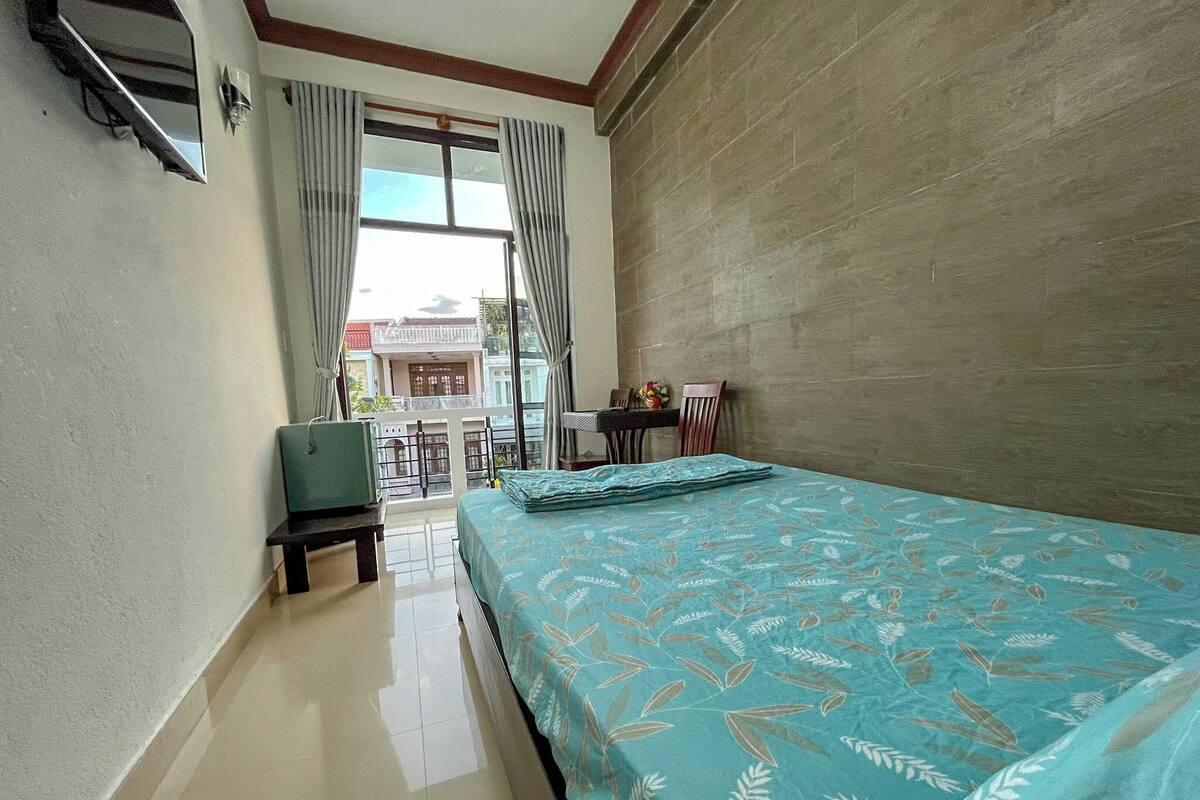 Habitación de hotel con cama, una pequeña mesa con sillas, escritorio y ventana con cortinas.