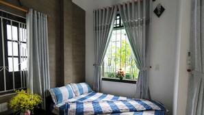 Quarto com cama, cortinas, janela com vista para o verde e um vaso com flores.