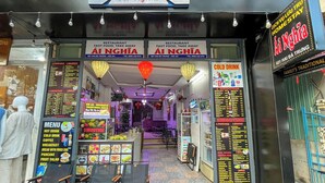 Um restaurante de comida rápida chamado Ai Nghia, com cardápio e mesas ao ar livre.