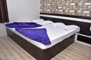 Una cama individual con un colchón blanco y una manta morada, una almohada blanca y un teléfono negro sobre una mesita de noche.
