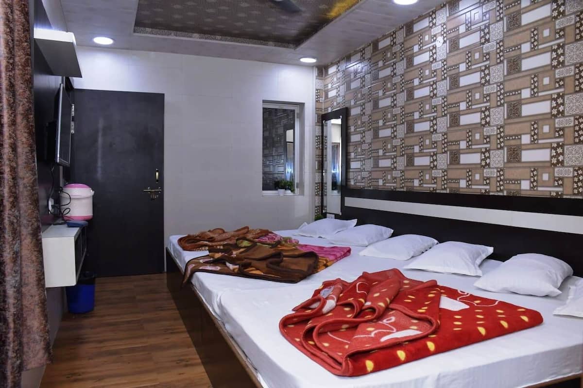 A hotel room with two beds, a small desk with a computer, a mirror, and patterned wallpaper.