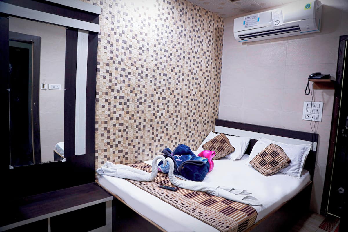 A hotel room with a bed, a bedside table, a mirror, an air conditioning unit, and a wall-mounted phone.
