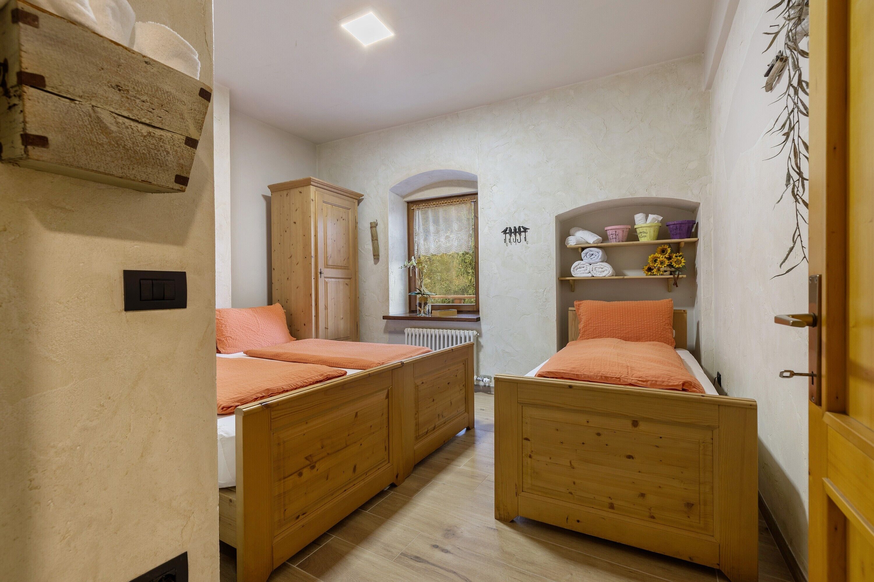 Ein Schlafzimmer mit zwei Holzbetten, einem Schrank aus Holz, einem Heizkörper und einem Regal mit Handtüchern und Pflegeartikeln.