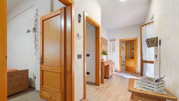 Un pasillo con puertas de madera, una pequeña mesa con una pila de libros y un armario de madera.