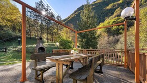 Un espacio de descanso al aire libre con bancos y una mesa, rodeado por una valla de madera, con montañas al fondo.