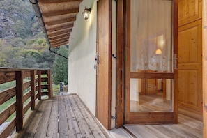 Une terrasse en bois avec une porte vitrée donnant sur une pièce offrant une vue sur un paysage montagneux.