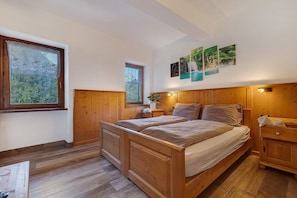 Une chambre à coucher avec un cadre en bois, comprenant un grand lit, une table de chevet, une commode et une fenêtre donnant sur un paysage verdoyant.