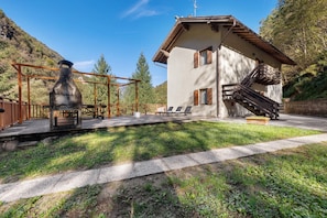 Un chalet doté d’une cheminée en pierre, d’une terrasse en bois et d’un escalier menant à un balcon.