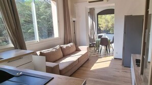 Et moderne, lyst værelse med en beige sofa, et spisebord med stole og et køkkenområde.