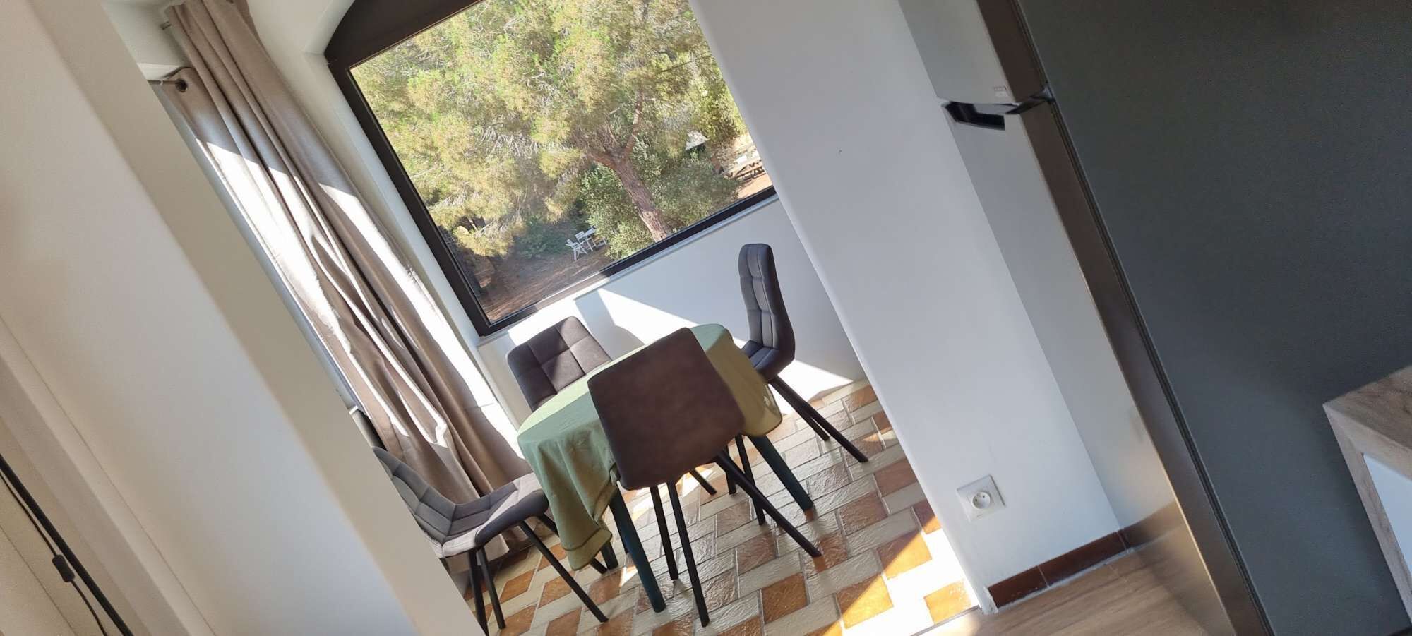 Un comedor con una mesa y sillas, una ventana con cortinas y vistas a árboles.