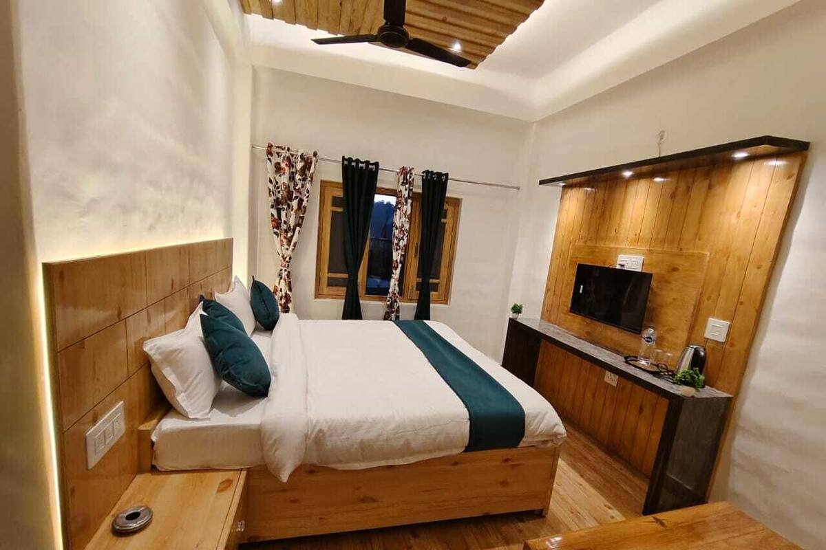 A modern bedroom with a wooden bed, a small bedside table, a built-in TV, and a wooden desk.