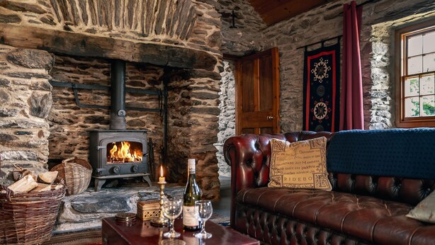 Une pièce aux murs de pierre, dotée d’une cheminée, d’un canapé en cuir et d’une table en bois sur laquelle se trouvent des verres et une bouteille.