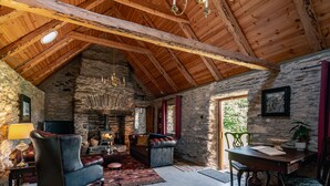 Une pièce rustique avec une cheminée en pierre, des poutres apparentes, des meubles en cuir et un lustre.