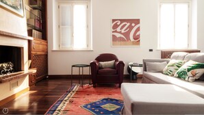 Un soggiorno con camino, una poltrona rossa, un divano, un tappeto decorato e un poster di Coca-Cola al muro.