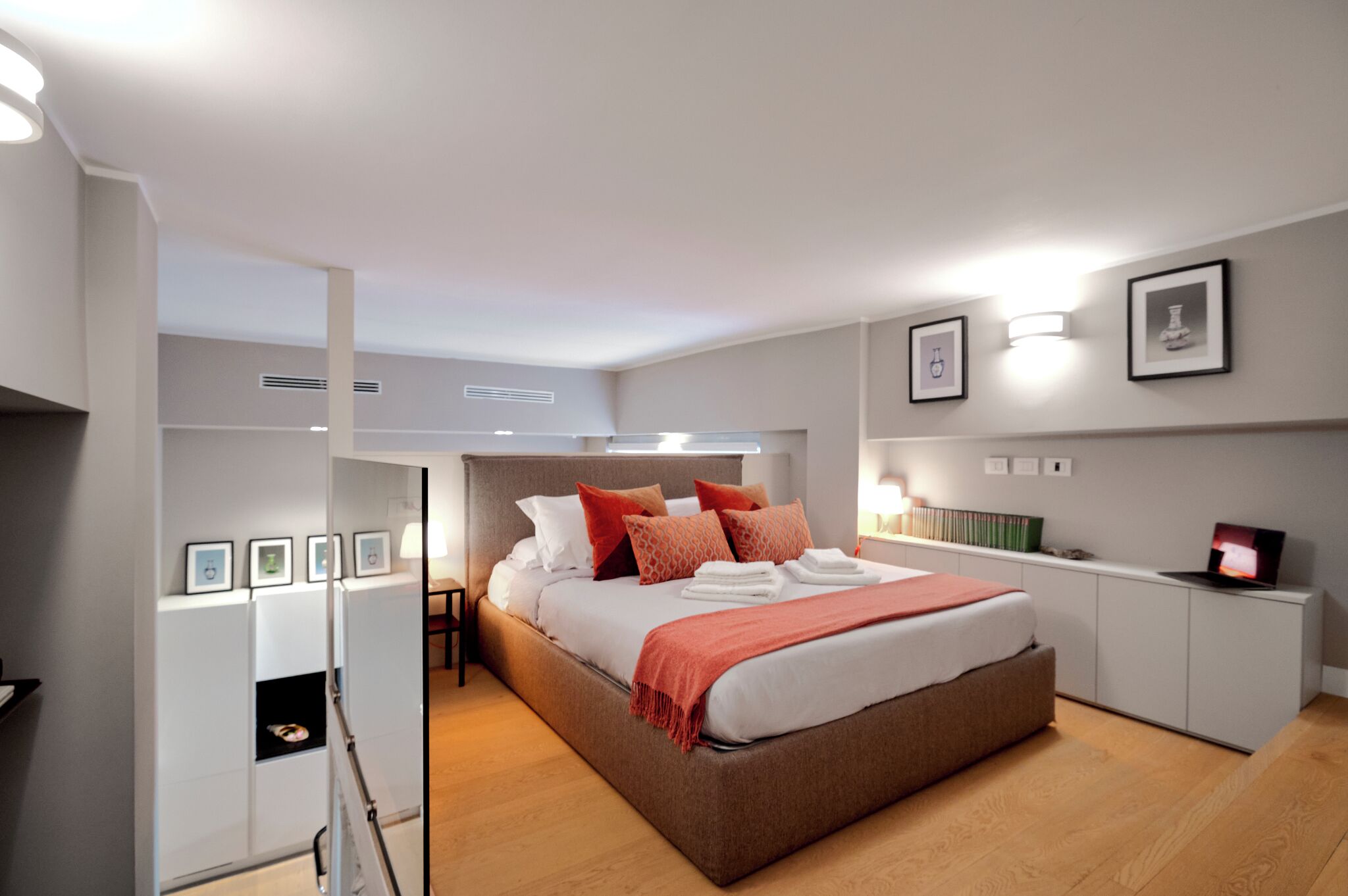 A modern bedroom with a large bed, bedside tables, a wardrobe, and framed pictures on the wall.
