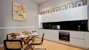 A modern kitchen with white cabinets, a black countertop, and a dining area with wicker chairs. - Milan Style (Milan)