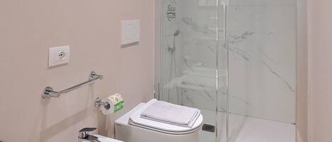 Un baño moderno con bidé, inodoro y ducha con mampara de vidrio.