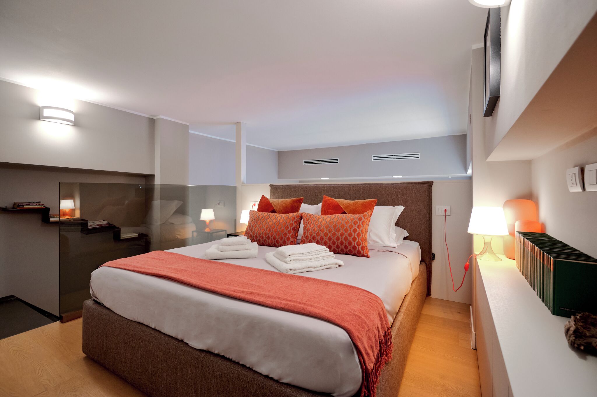 A modern hotel room with a large bed, a bedside table, a nightstand, a mirror, and a wall-mounted TV.