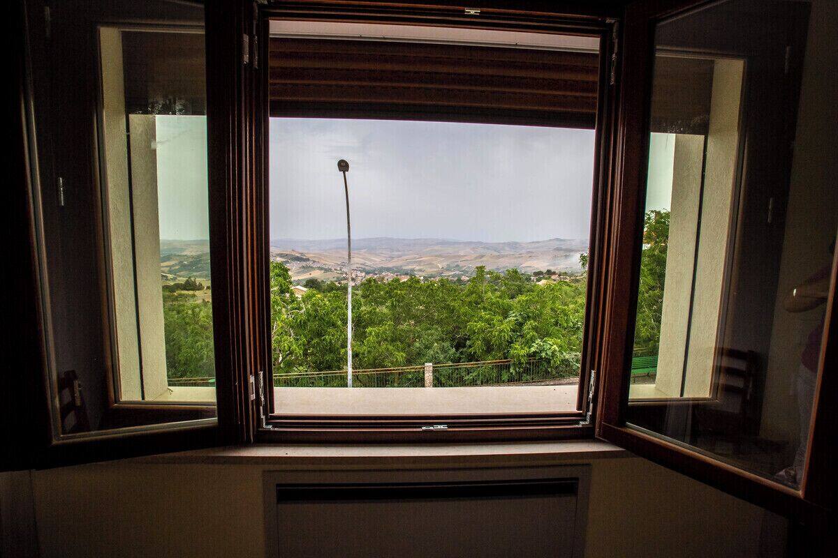 Een kamer met een groot raam dat uitzicht biedt op een groen landschap en verre heuvels.