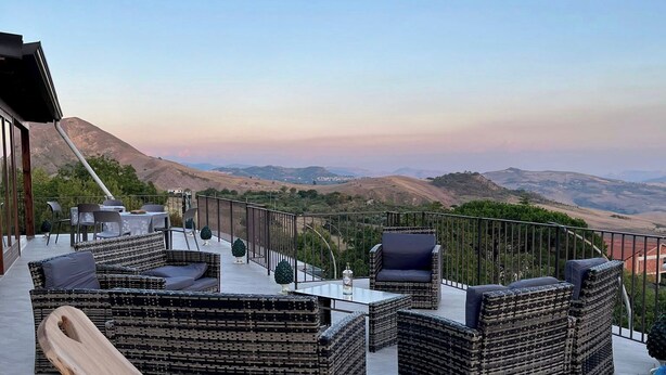 Une terrasse sur le toit, aménagée avec des meubles en osier, une table en bois et une bouteille de gel hydroalcoolique.
