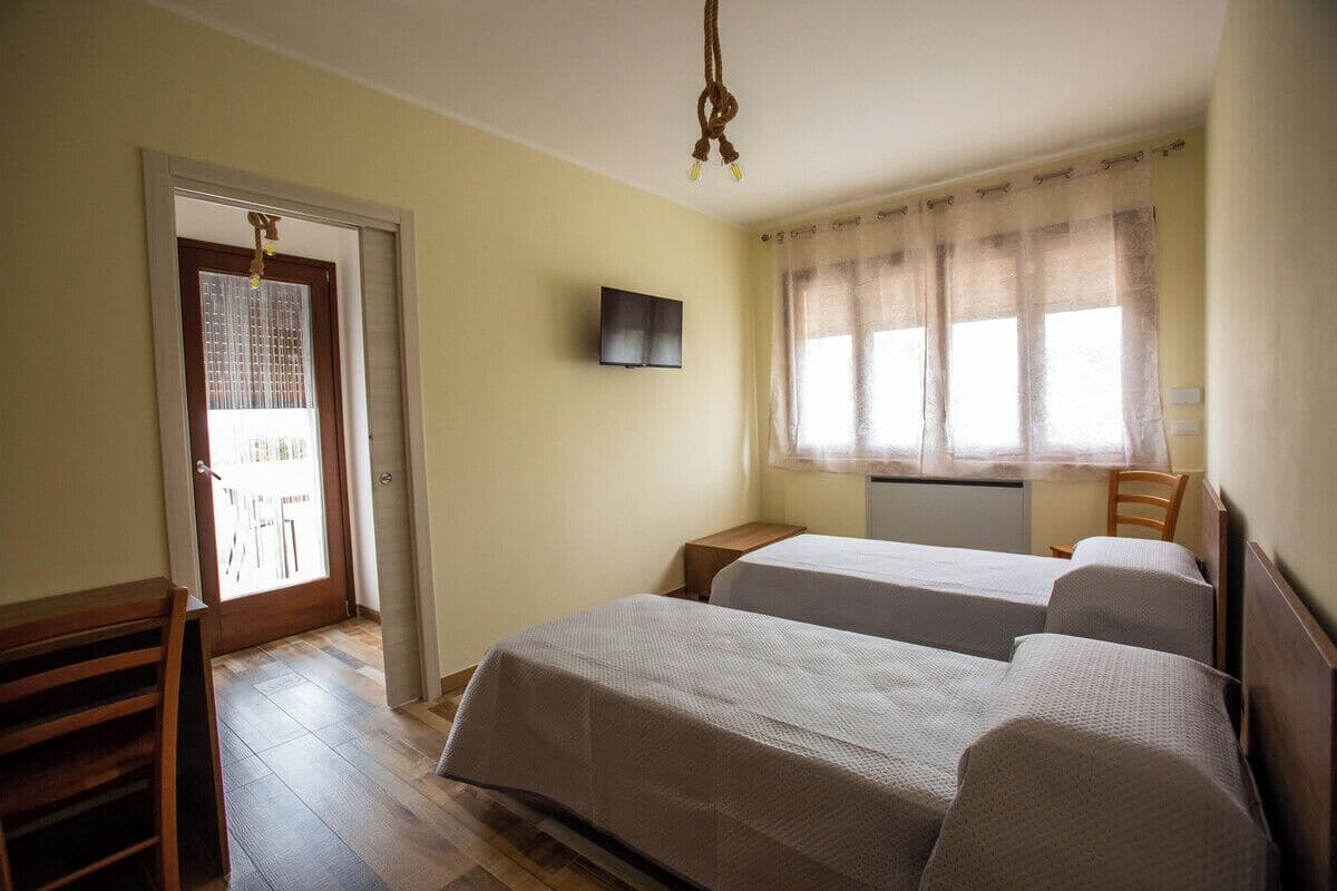 Een kamer met twee bedden, een televisie, een raam met gordijnen en een deur naar buiten.