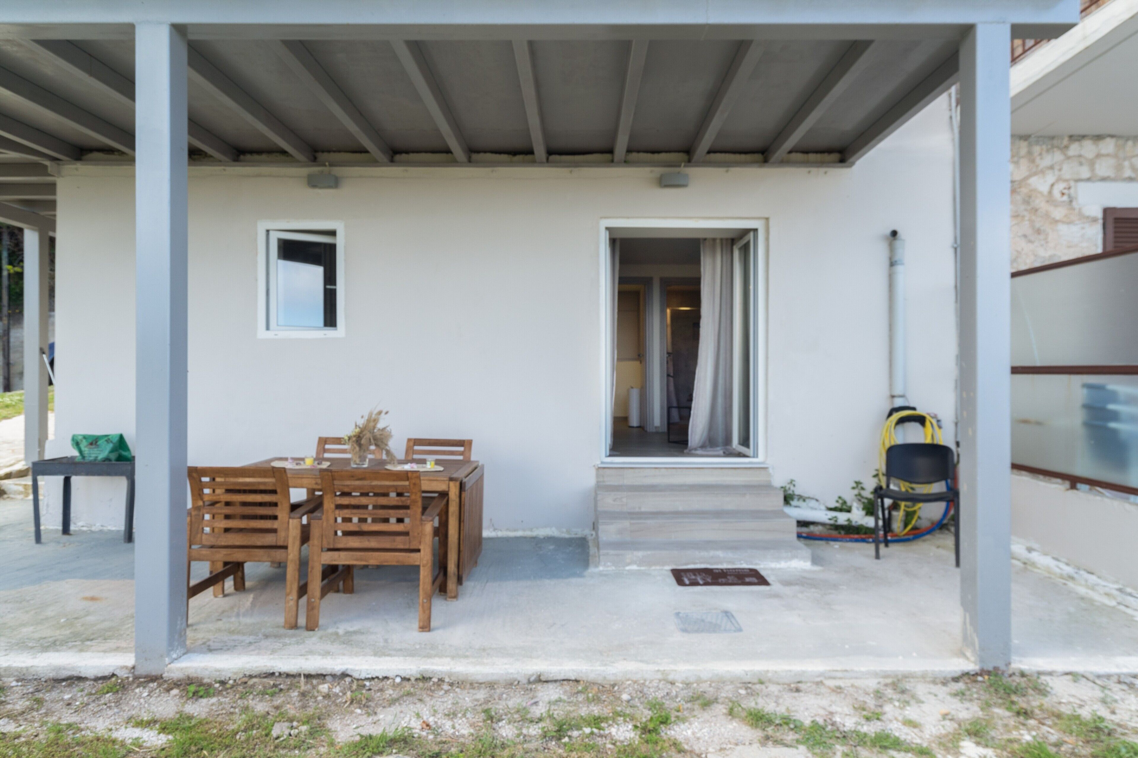 Un espace extérieur abrité, aménagé avec une table et des chaises, une petite fenêtre et une porte donnant sur un espace intérieur.