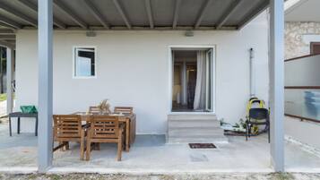Un espace extérieur abrité, aménagé avec une table et des chaises, une petite fenêtre et une porte donnant sur un espace intérieur.
