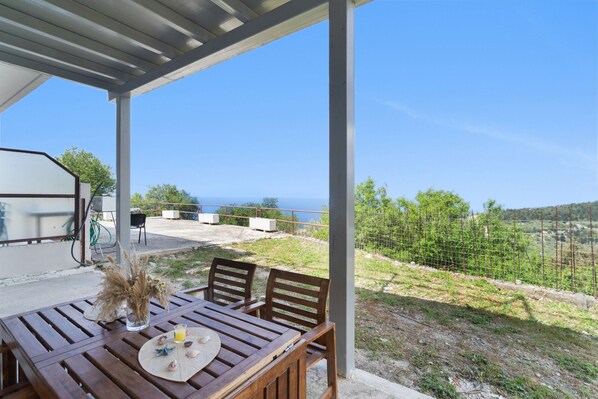 A wooden table with chairs and a vase of dried flowers, set under a covered patio with a view of the sea. - Country House 'Villa Andreas' with Sea View, Private Terrace and Wi-Fi (Athani)