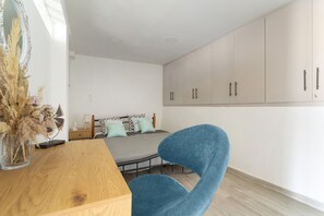 Um quarto com cama, escrivaninha de madeira, cadeira, espelho e guarda-roupa.