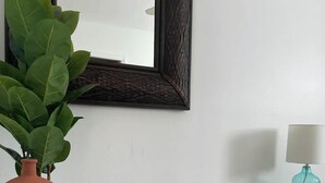 Et hvidt kommode med tre skuffer, et spejl over, en terracotta-vase med en plante, og en teal-farvet lampe på kommoden.