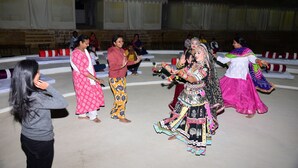 Un grupo de personas vestidas con atuendo tradicional bailando sobre un escenario, con carpas al fondo.