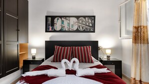 Habitación de hotel con una cama grande, dos almohadas, una obra de arte colgada en la pared, dos mesitas de noche con lámparas y una cortina.