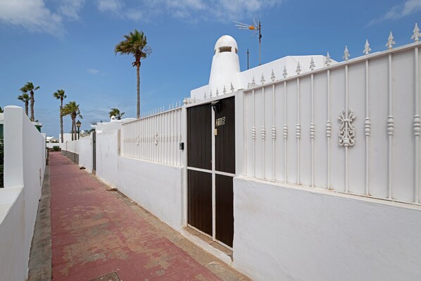 A white building with a black door marked '21B,' a red pathway, and palm trees.