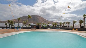 Piscina con sillones de descanso y palmeras, con montañas al fondo.