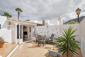 Un patio con una mesa y sillas, una planta en maceta y una pared decorada con platos.