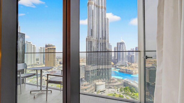 A balcony with a view of a tall skyscraper, a table, and a chair. - WYZ RENT|3 BDs Address Opera-Burj Khalifa (Dubai)