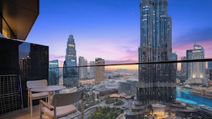 A balcony with a table and chairs overlooking a cityscape with modern skyscrapers and a river. - WYZ RENT|3 BDs Address Opera-Burj Khalifa (Dubai)
